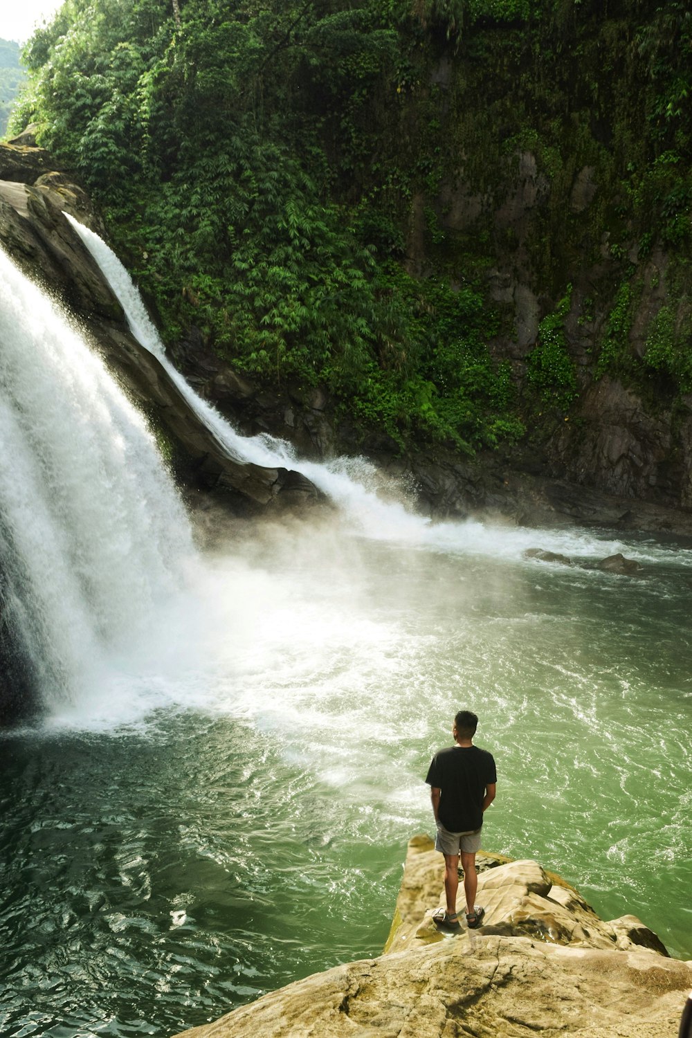 a man standing on a rock in front of a waterfall