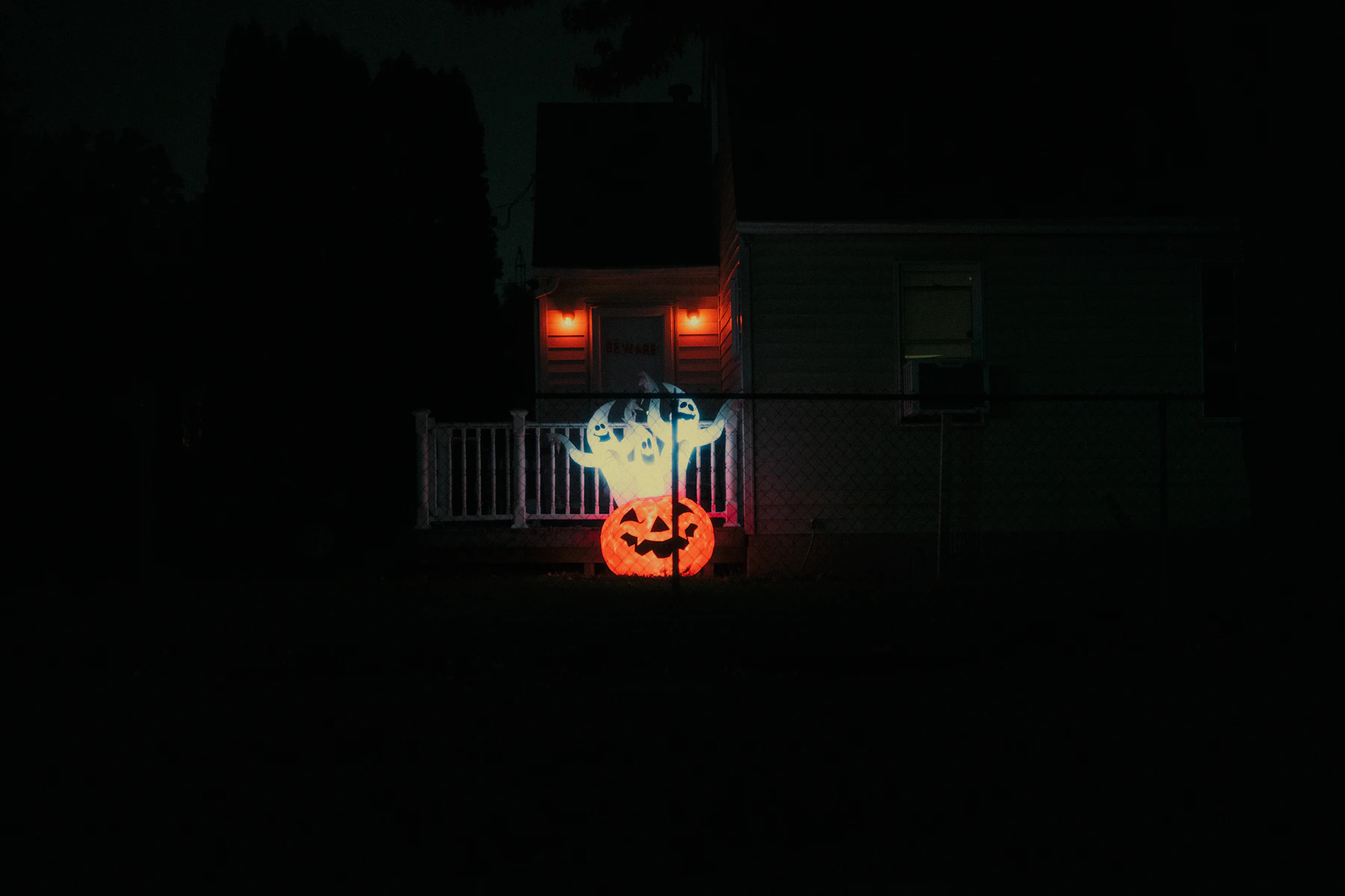A lit jack-o-lantern glowing outside a house in the dark