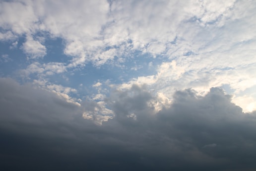 Cloudy sky featuring a mix of cumulus and stratus clouds with patches of blue sky peeking through. The light from the sun subtly illuminates the edges of the clouds, creating a dynamic contrast between the bright and shadowed areas.