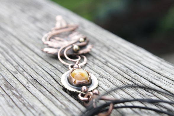 Close-up of a handcrafted Mexican jewelry piece resting on natural wood with soft sunlight.