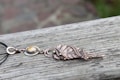 A handcrafted necklace with an intricate design lies on a weathered wooden surface. The necklace features a metal pendant with leaf motifs and a polished stone centerpiece. The metal has a warm, coppery tone with a delicate chain attached.