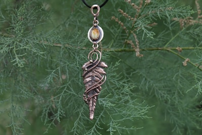 Handmade crow-inspired pendant resting on a bed of pine needles.
