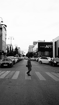 Black and white photo of a crowded urban street with people crossing and vintage cars.