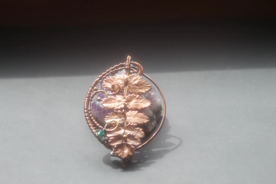 Close-up of a handcrafted matte copper pendant with vintage patina on a minimalist background