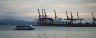 Cargo being loaded onto an offshore supply ship with cranes against a sunset backdrop.