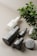 A collection of minimalist skincare or cosmetic bottles in sleek black and white designs. These are arranged on a soft, neutral-colored surface with a green plant branch and a few decorative stones placed nearby, adding a natural element to the composition.
