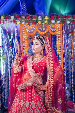 A festive setting with a Bengali bride wearing a red-bordered Bengal Tant saree, adorned with floral alpana motifs in the background.