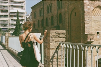 a woman in a black dress is standing on a bridge