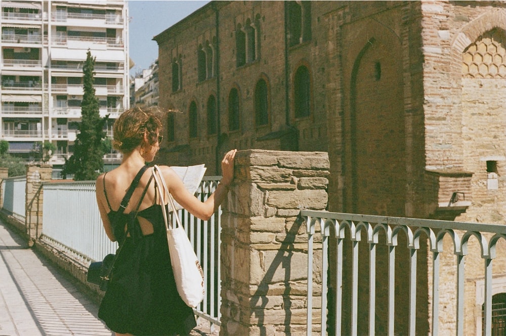 a woman in a black dress is standing on a bridge