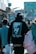 A person wearing a black hoodie with an image of a famous musician and the words 'Until The End of Time' on the back is walking in a busy outdoor urban setting. The street is bustling with multiple people, and there are shops and colorful signs in the background.