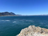 A traveler capturing a panoramic view from a cliff overlooking a vast ocean.