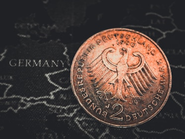 A close-up of a 2 Deutsche Mark coin featuring the German eagle emblem, placed over a map with the word 'Germany' visible.