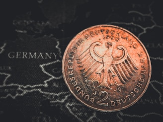 A close-up of a 2 Deutsche Mark coin featuring the German eagle emblem, placed over a map with the word 'Germany' visible.