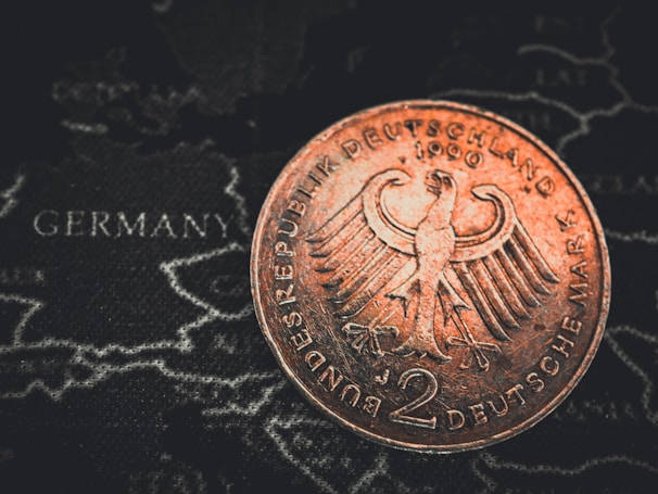 A close-up of a 2 Deutsche Mark coin featuring the German eagle emblem, placed over a map with the word 'Germany' visible.