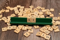 Scattered wooden letter tiles on a wooden surface, with a green tile holder displaying the letters 'A' and 'I' prominently in the center.