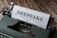 A vintage typewriter with a sheet of paper loaded, displaying the word 'DEEPFAKE' in bold letters. The typewriter sits on a wooden surface, adding a rustic touch to the image.