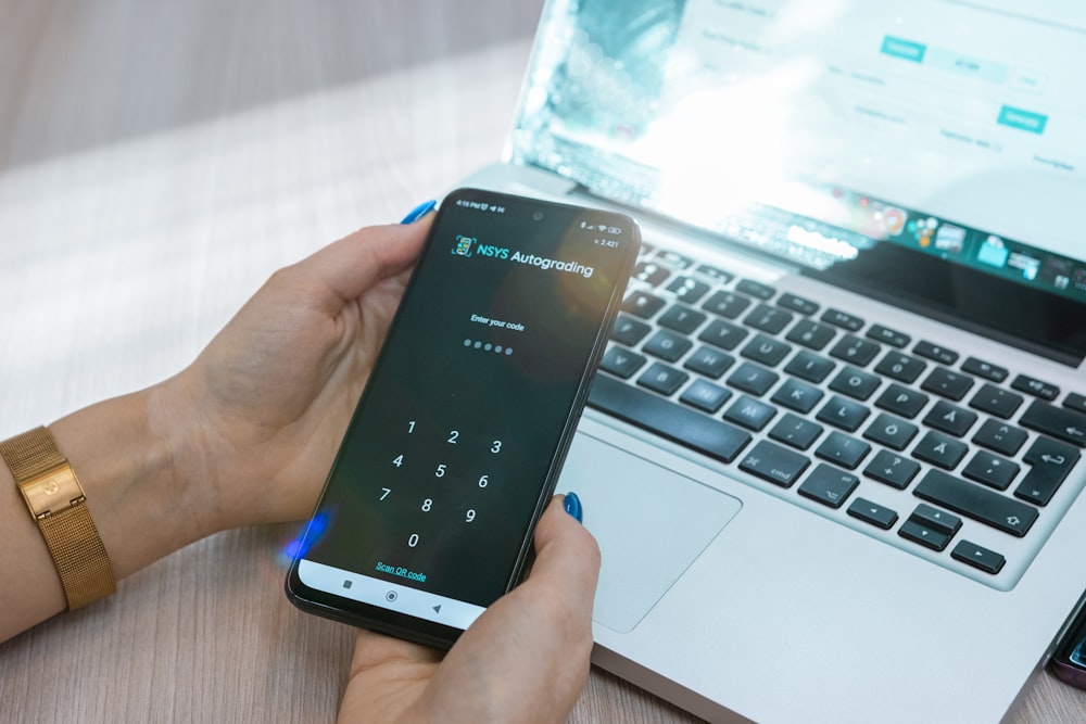 a person holding a cell phone in front of a laptop