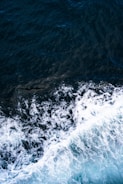 Waves of the ocean with foamy white crests crash against the dark blue water surface, creating a sense of motion and energy.