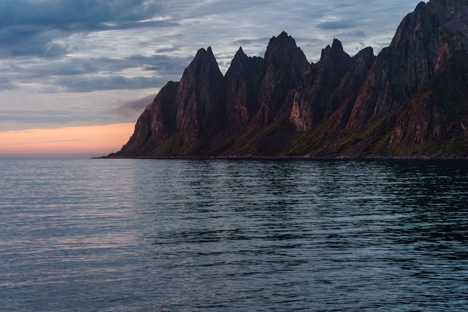 Serene coastal scene at sunset with mountains behind and calm ocean stretching to horizon