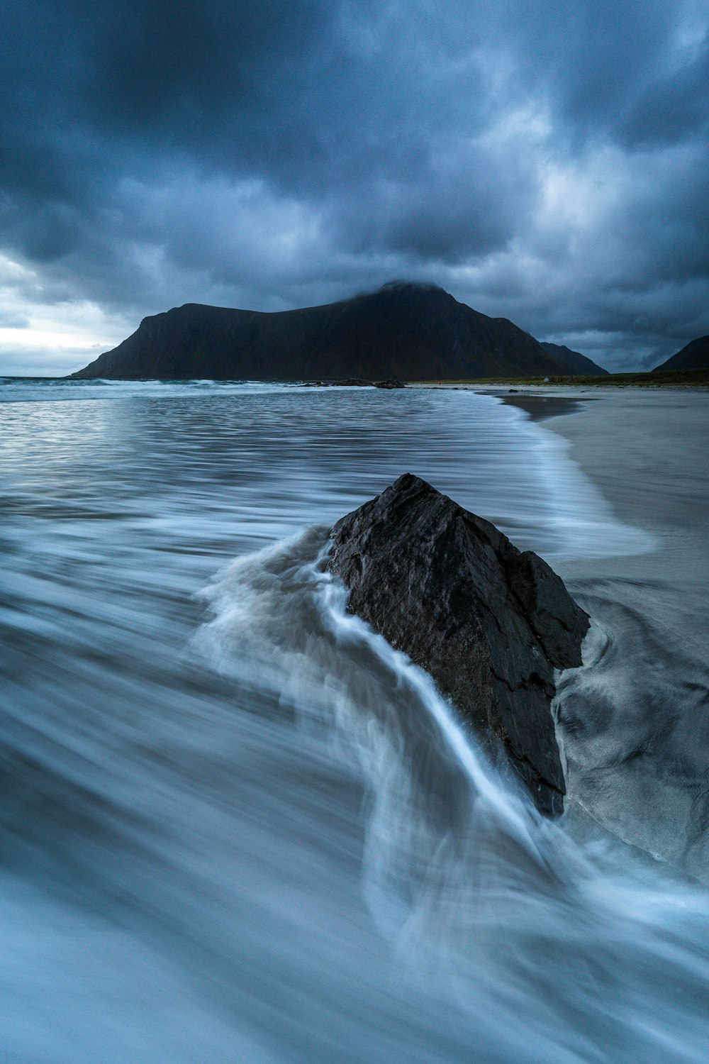 a large rock sitting on top of a beach under a cloudy sky