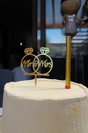 Close-up of a delicate 3D printed gold cake topper resting on a white frosted cake, with soft natural light highlighting its fine details.