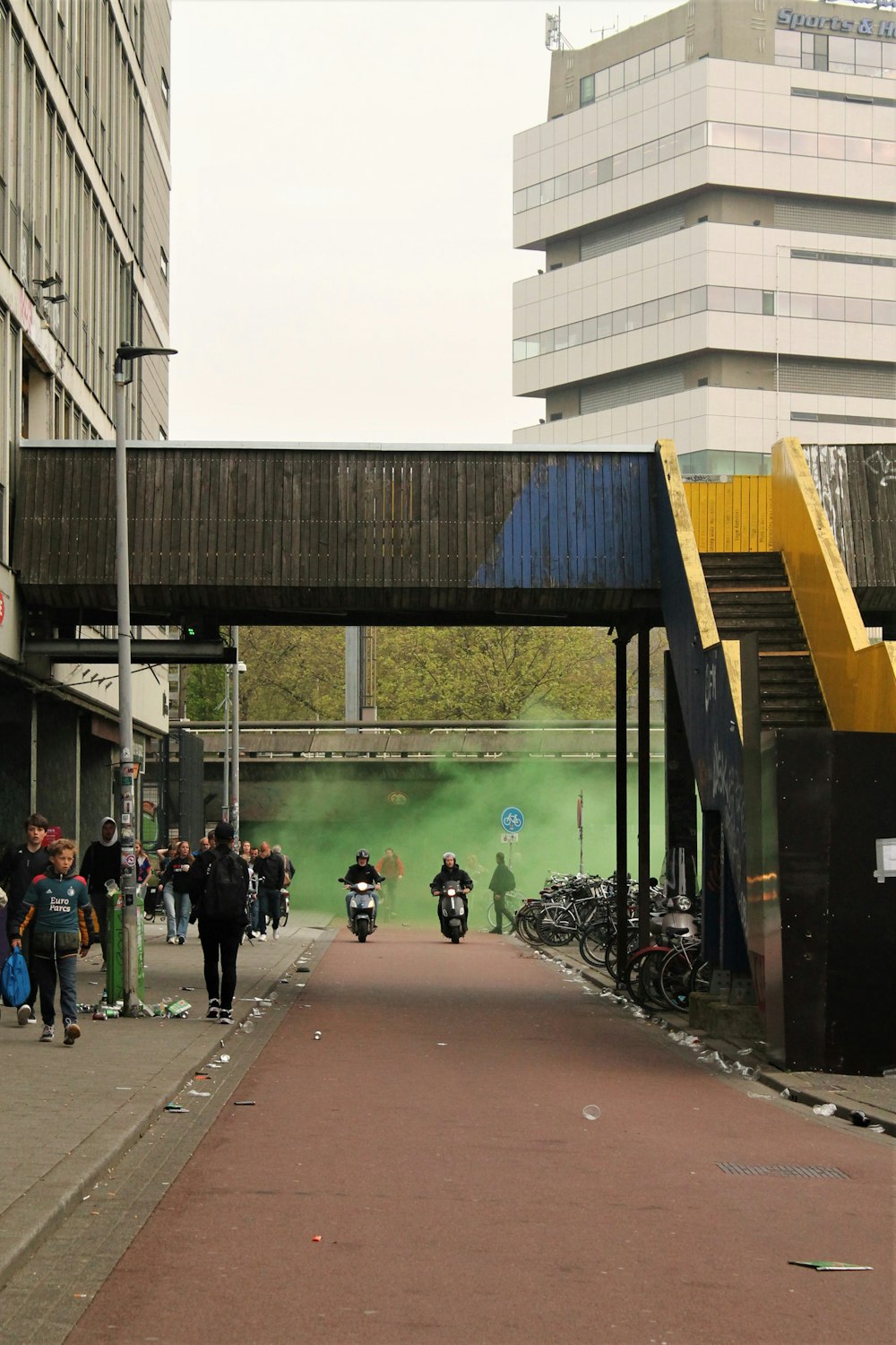 a group of people walking down a sidewalk under a bridge