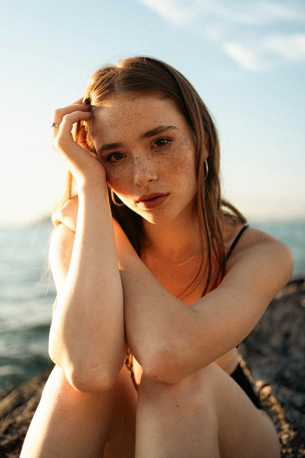 a woman sitting on a rock by the water