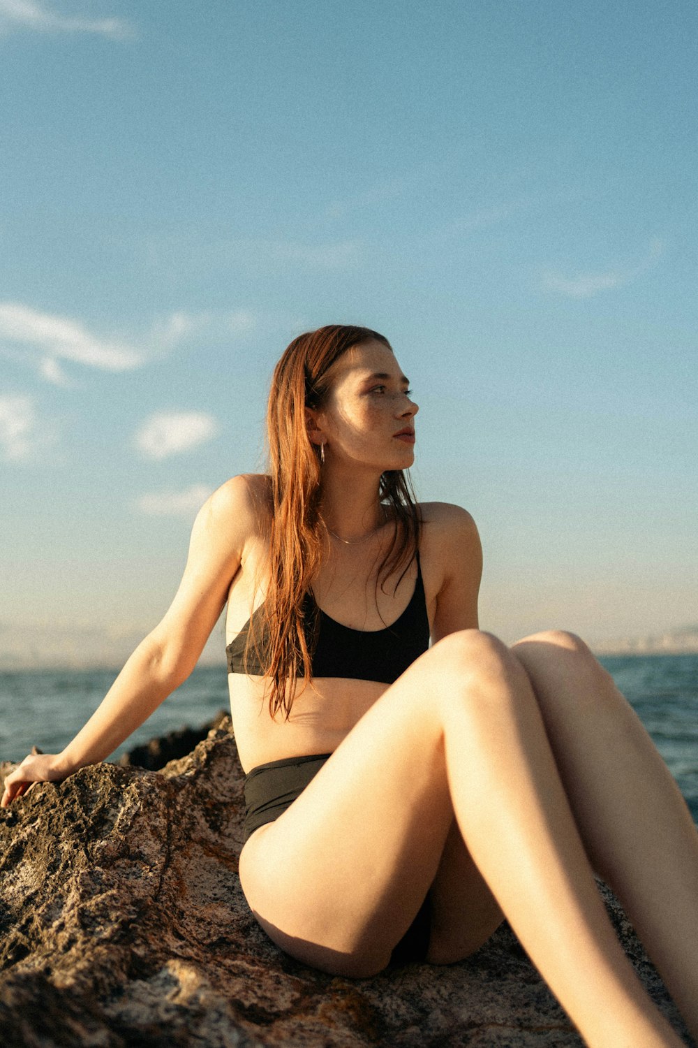 a woman sitting on top of a rock next to the ocean