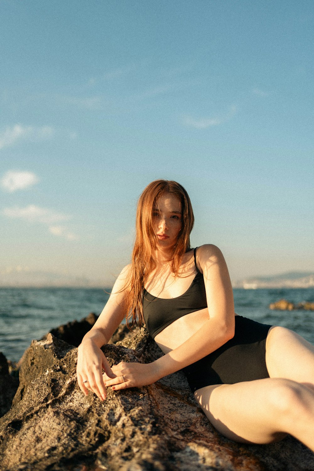 a woman sitting on a rock near the ocean