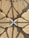 An intricate architectural canopy with geometric patterns and shadows. The structure forms a symmetrical design with a mix of straight lines and curves, creating a flower-like shape in the center. The material appears translucent, allowing sunlight to cast intricate shadows.