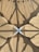 An intricate architectural canopy with geometric patterns and shadows. The structure forms a symmetrical design with a mix of straight lines and curves, creating a flower-like shape in the center. The material appears translucent, allowing sunlight to cast intricate shadows.