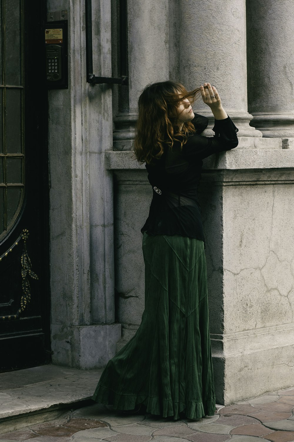 a woman in a long green skirt leaning against a wall