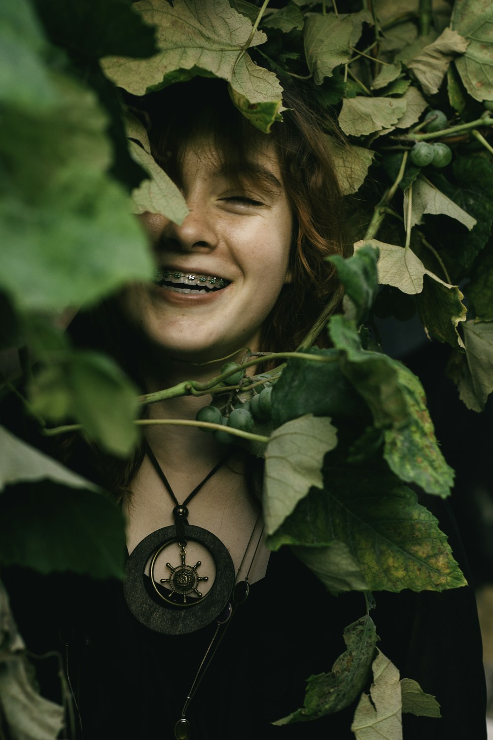 a woman is smiling while hiding behind some leaves