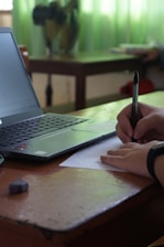 a person writing on a piece of paper next to a laptop
