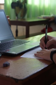 a person writing on a piece of paper next to a laptop