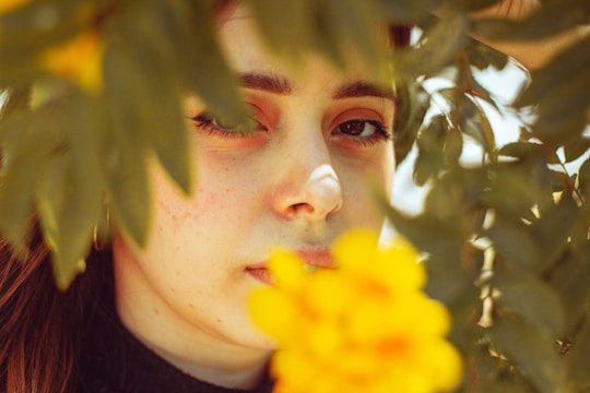 A close-up portrait of a woman smiling softly, surrounded by lush greenery.