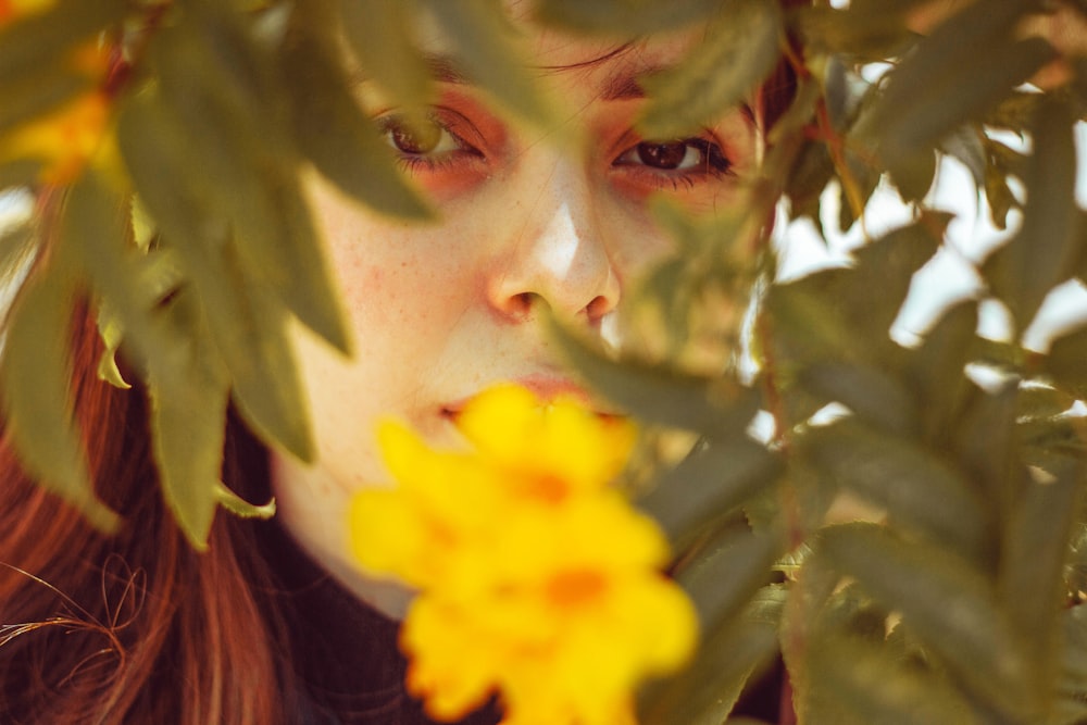 a woman with red hair and green eyes looking at a yellow flower