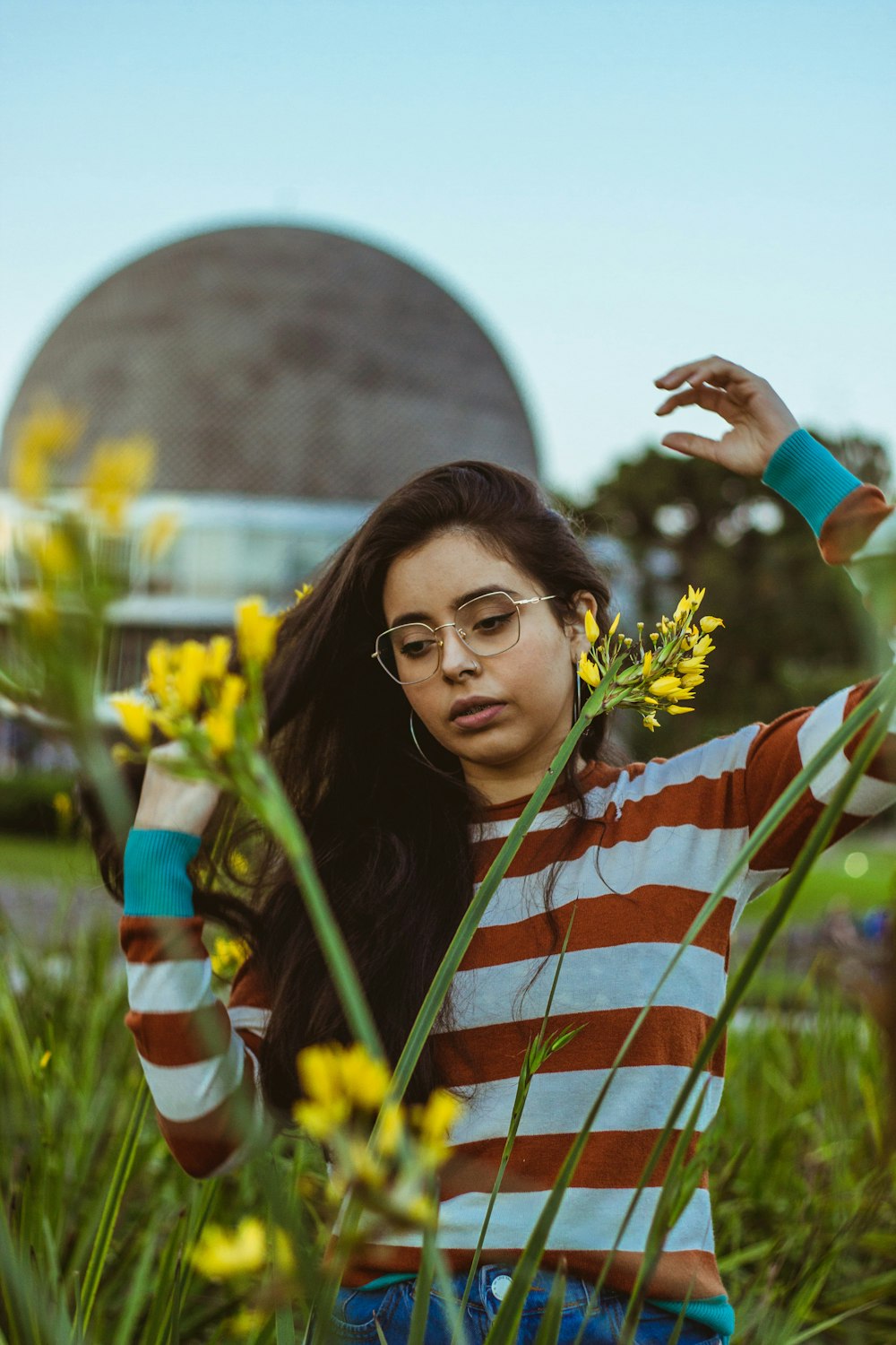 a woman with glasses standing in a field of flowers