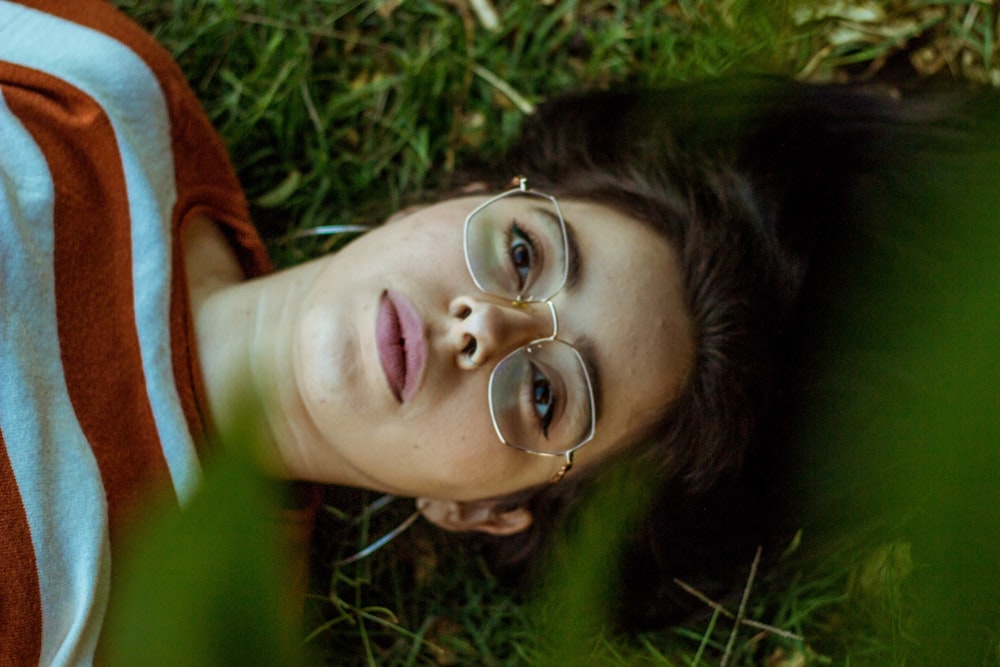a woman wearing glasses laying in the grass