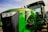 A large green agricultural tractor with the model number 8310 RT prominently displayed on its side. The vehicle features a robust build, with a visible engine compartment and modern headlights. The driver’s cabin is visible with clear windows, and the tractor is parked on a gravel surface under a partly cloudy sky.