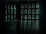 Rectangular light panels on a dark wall create an illuminated grid pattern. The room appears spacious with a reflective floor and minimal obstruction, exuding a futuristic or modern atmosphere.