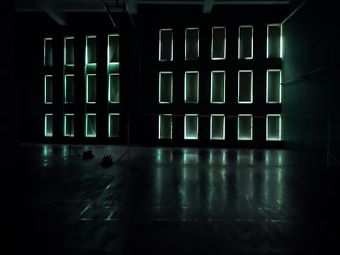 Rectangular light panels on a dark wall create an illuminated grid pattern. The room appears spacious with a reflective floor and minimal obstruction, exuding a futuristic or modern atmosphere.