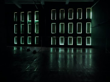 Rectangular light panels on a dark wall create an illuminated grid pattern. The room appears spacious with a reflective floor and minimal obstruction, exuding a futuristic or modern atmosphere.
