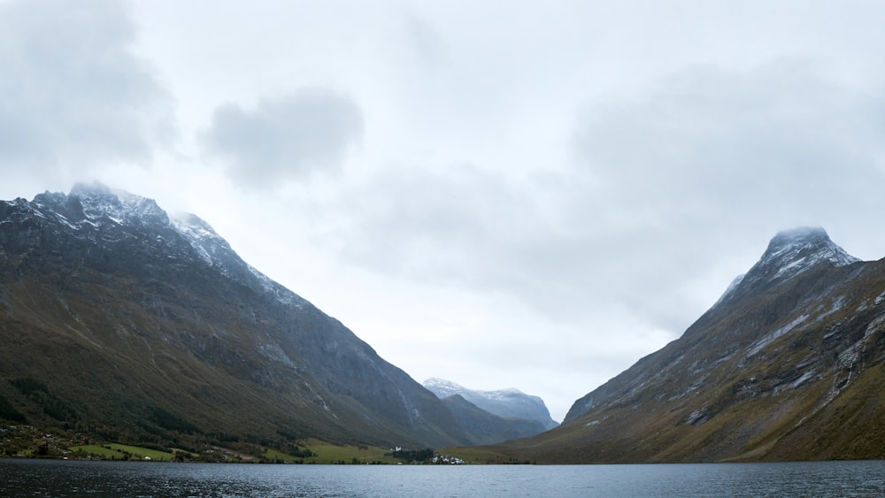 a body of water surrounded by mountains under a cloudy sky