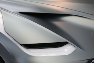 Close-up of a car's front design featuring sleek lines and a sharp, angular light element. The surface is smooth with modern styling and a glossy finish.