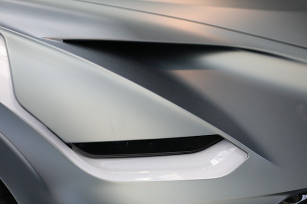 Close-up of a car's front design featuring sleek lines and a sharp, angular light element. The surface is smooth with modern styling and a glossy finish.