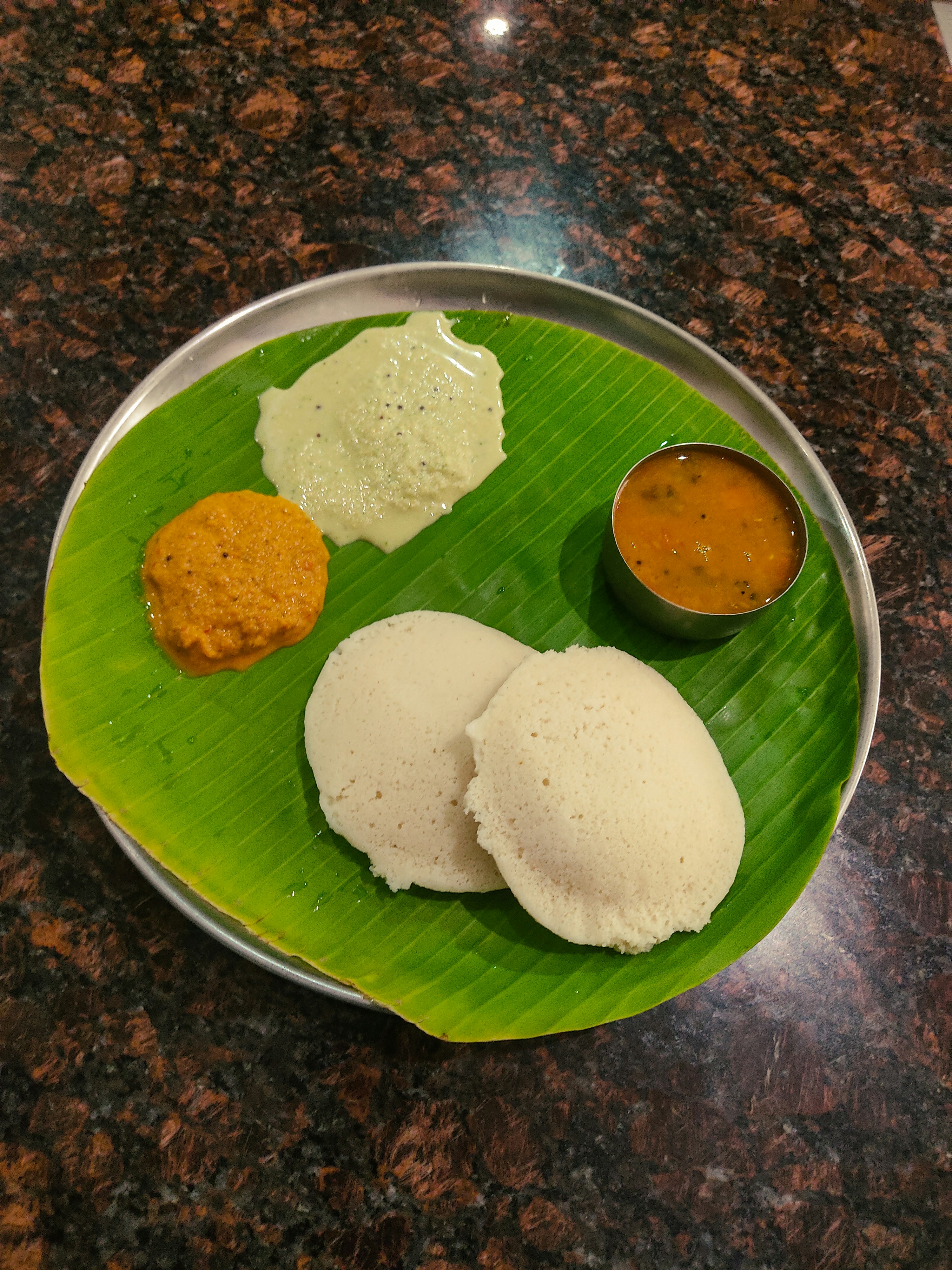 White steamed idlis with sambar and coconut chutney on banana leaf