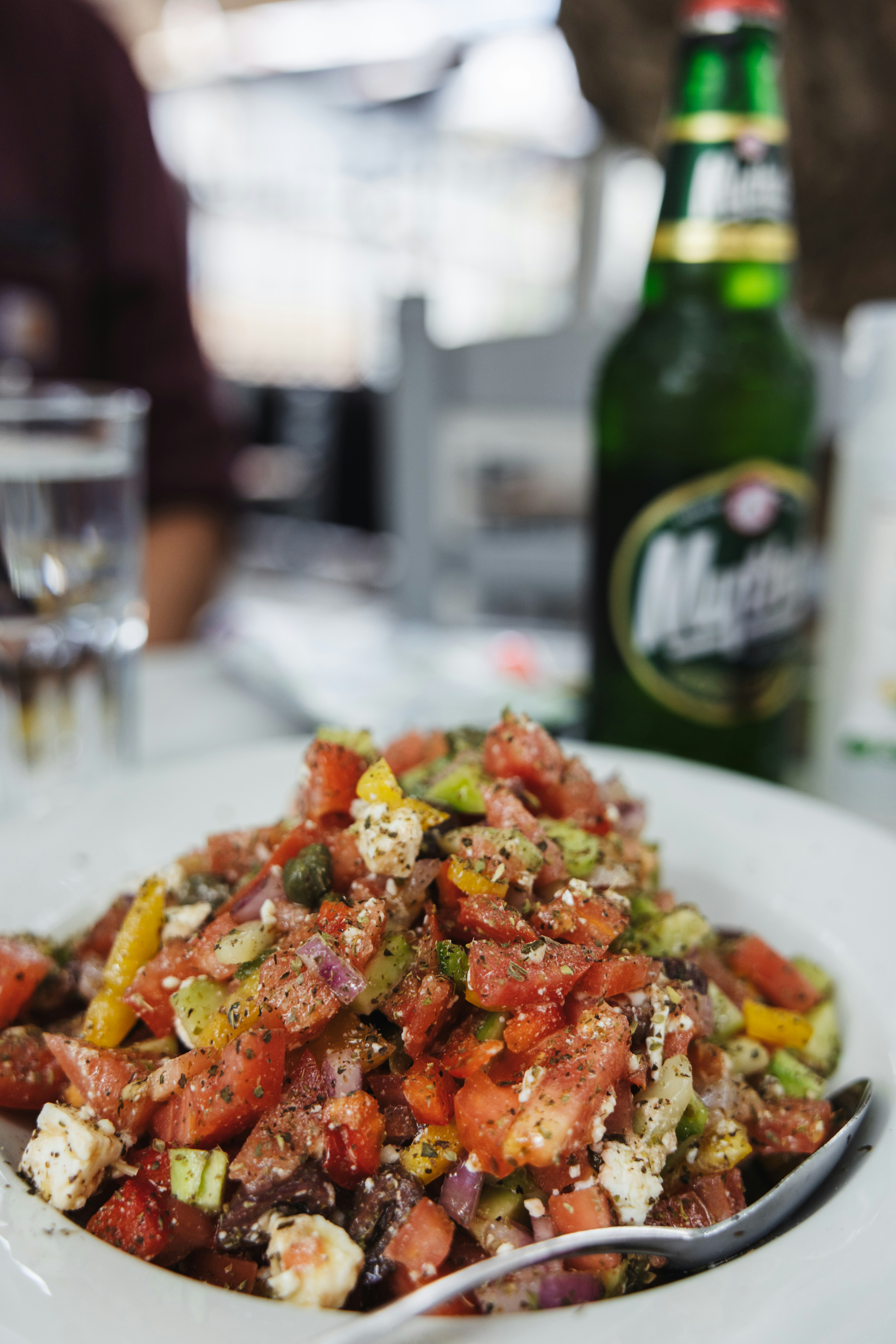 un plato blanco cubierto con una ensalada junto a una botella de cerveza