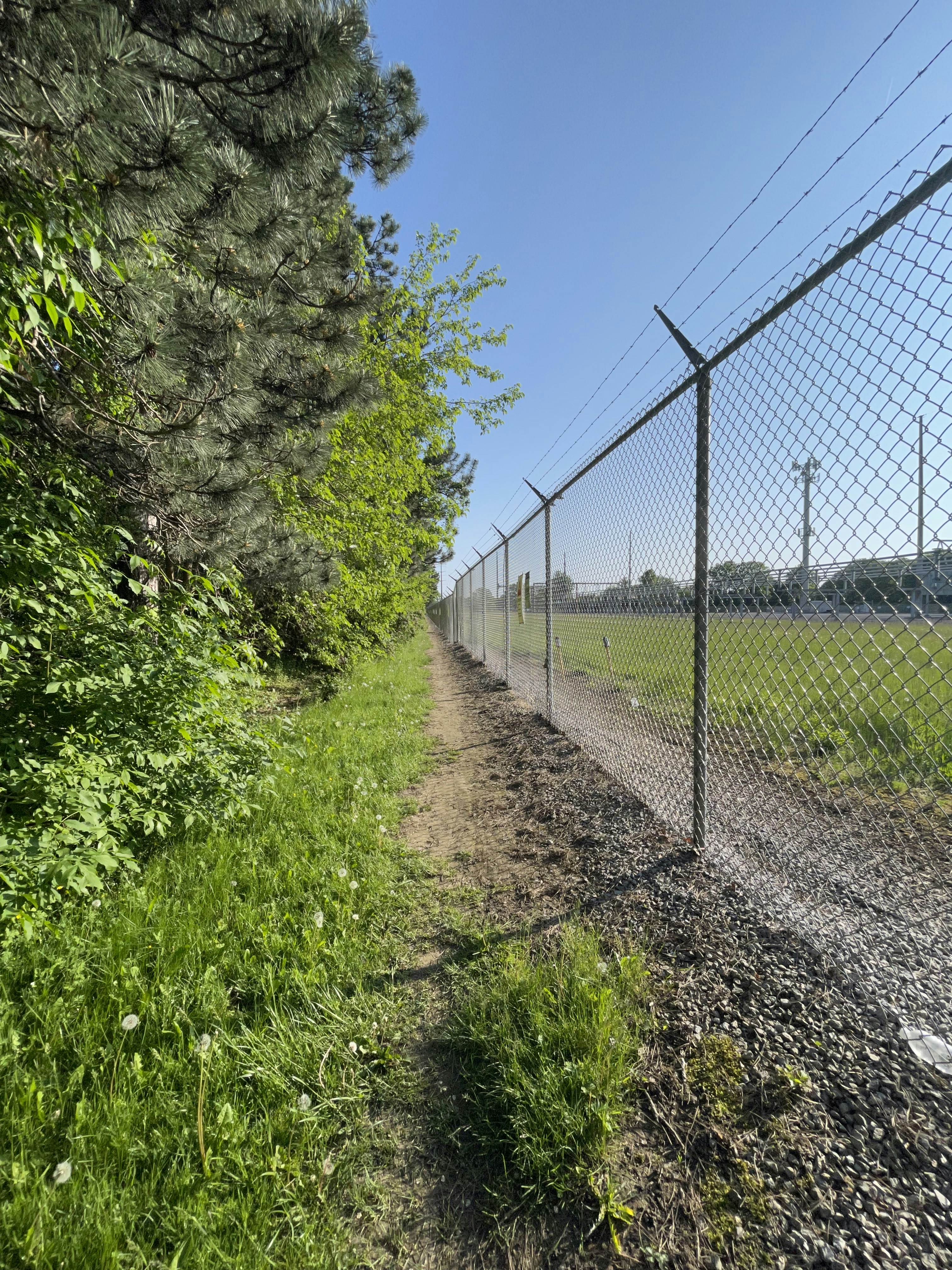 a dirt path next to a fence and a field