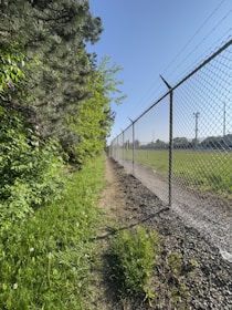 a dirt path next to a fence and a field